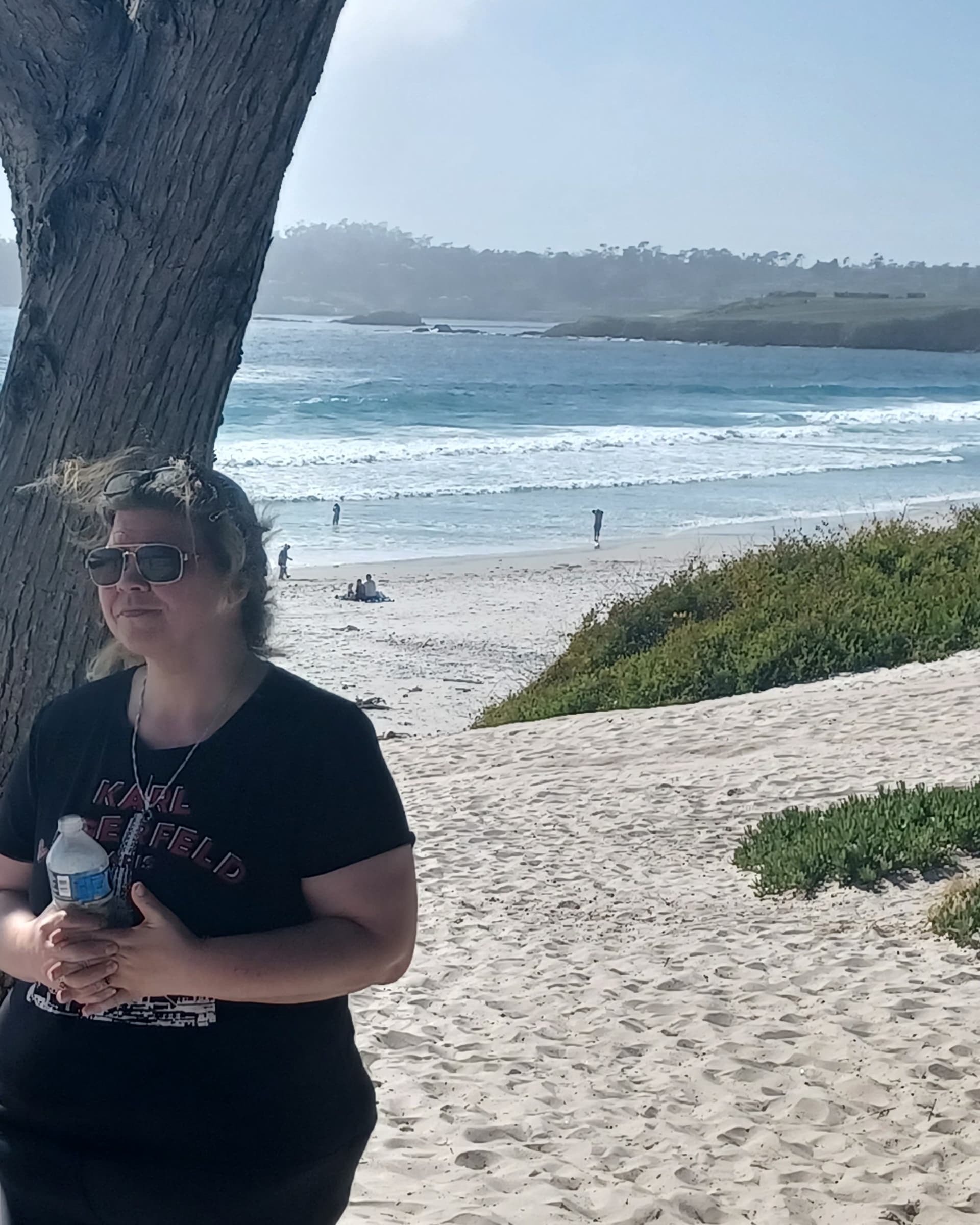 Mama Mystic standing against the cypress tree on Sunset Beach, Carmel-by-the-Sea — the shot to match